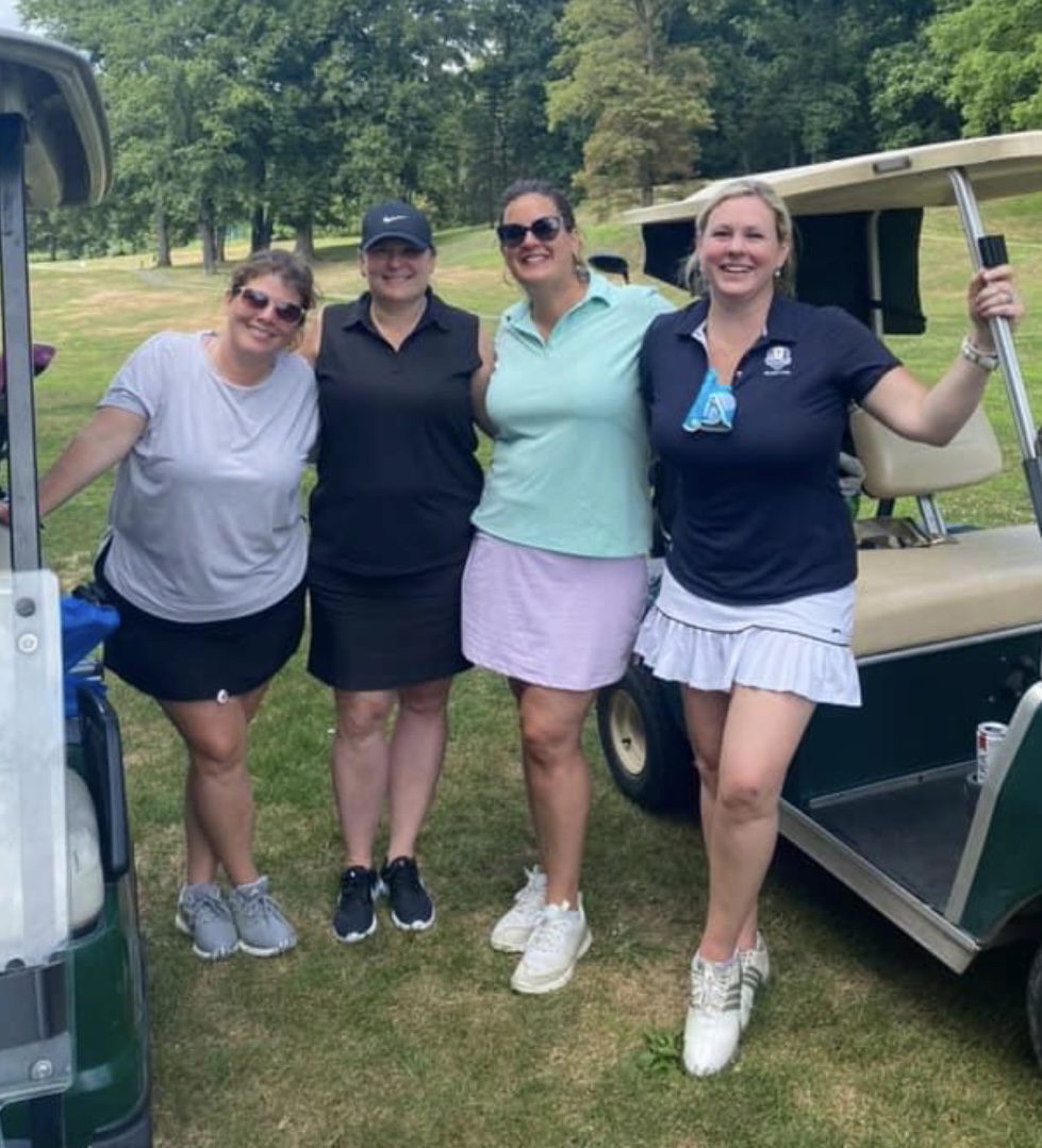 Four women are posing for a picture while standing next to a golf cart.