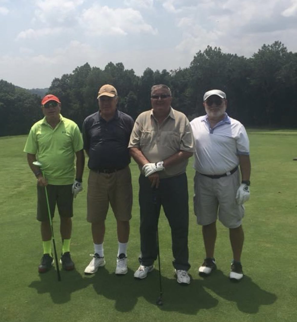 Four men standing on a golf course holding their clubs.