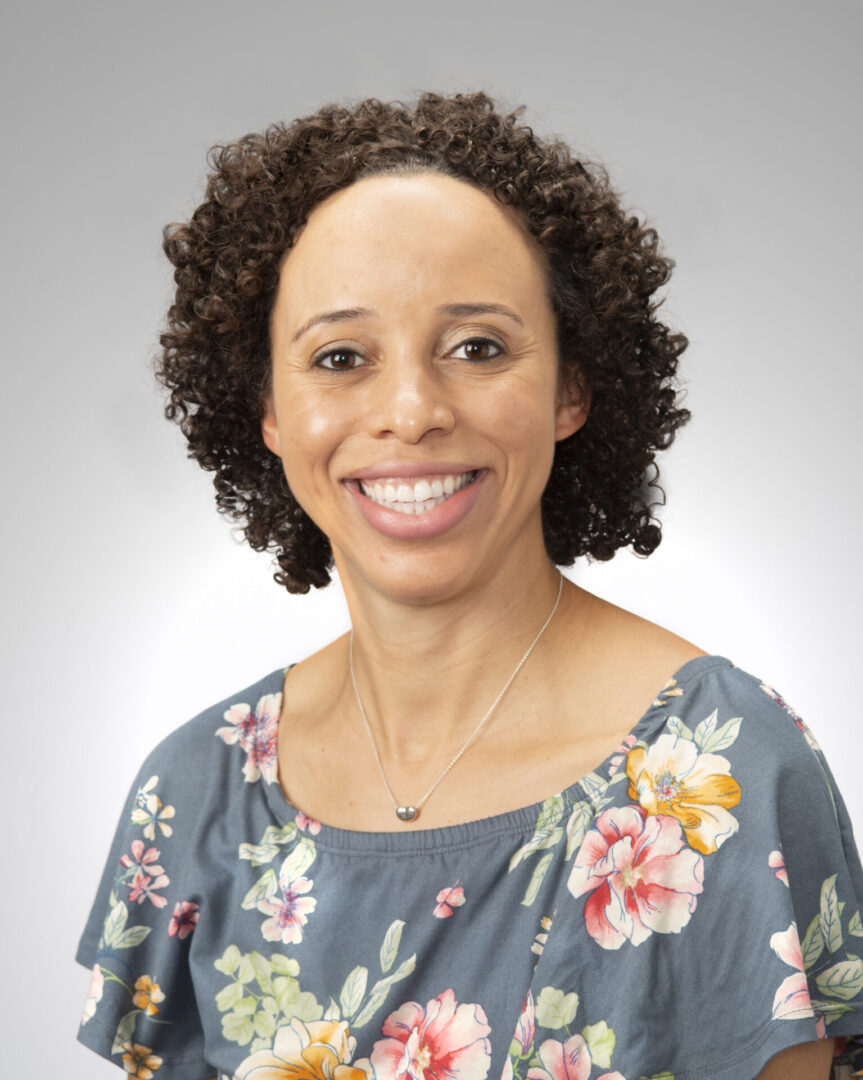 A woman with curly hair wearing a floral shirt.